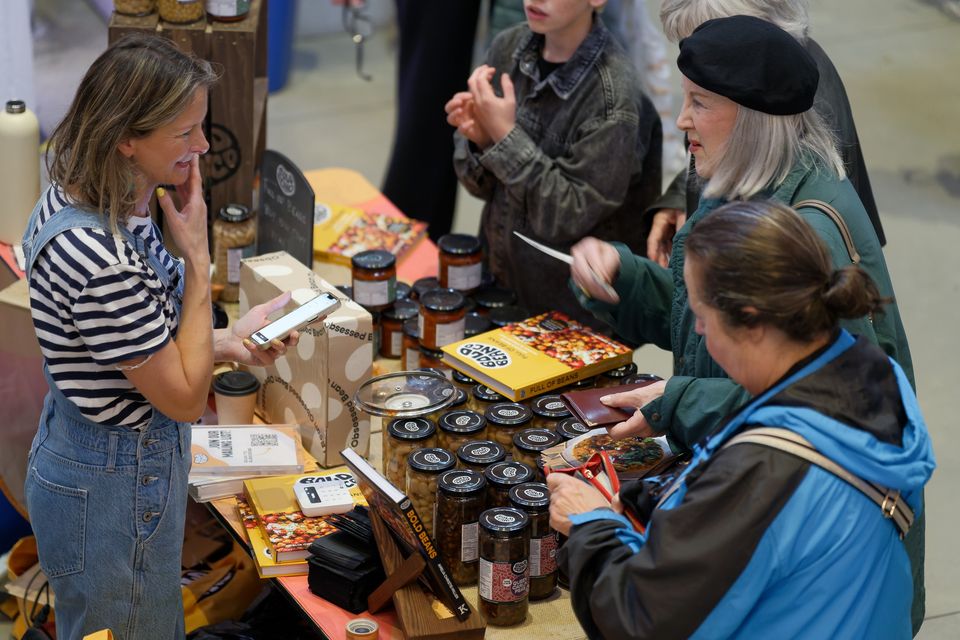 Visitors discussing jars of preserves at a market stall